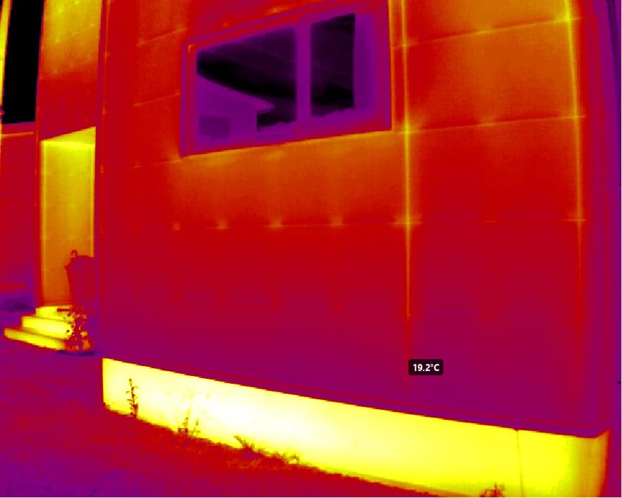 A facade where the window glass reflects the sky and the house opposite, appearing cold in the thermal image